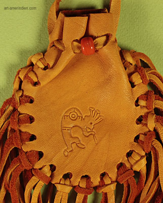 détail du symbole amérindien Kokopelli gravé sur ce medicine bag en cuir orné d'une perlle de verre et de nombreuses franges en lanières de cuir